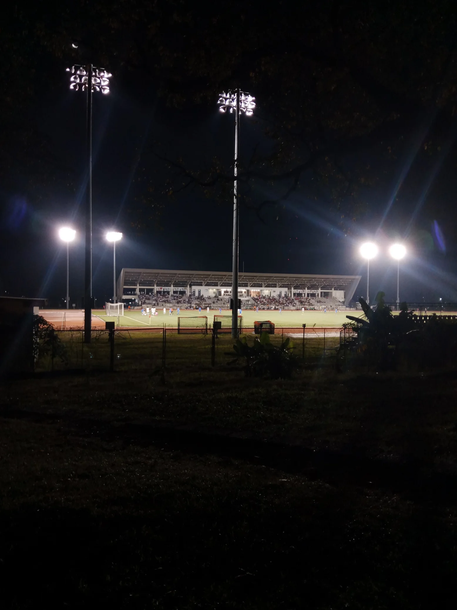 A football match under the stadium lights that night, seen from the far side of the pitch.